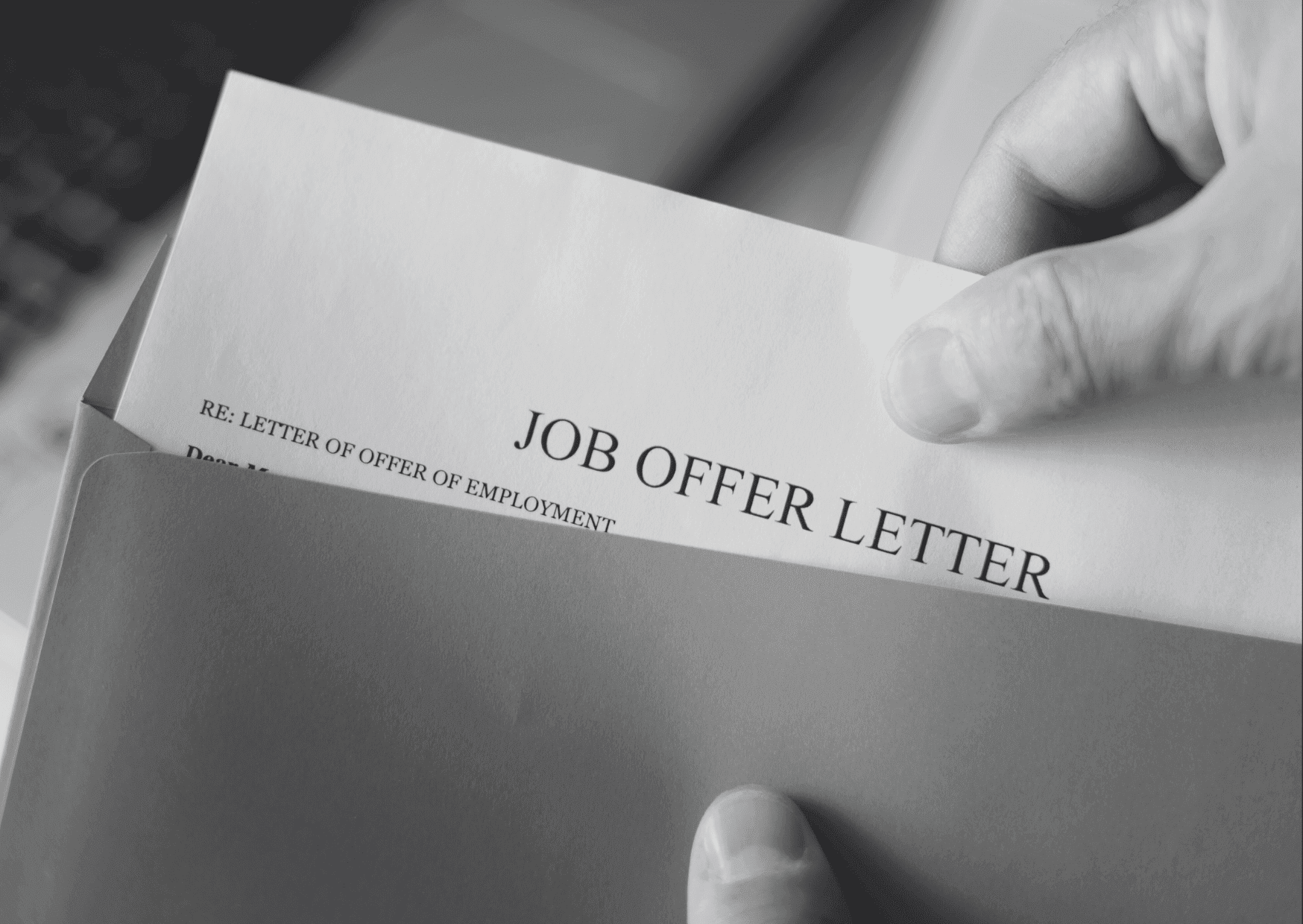 Close-up of a person's hands opening an envelope to reveal a formal 'JOB OFFER LETTER' printed in bold black text.