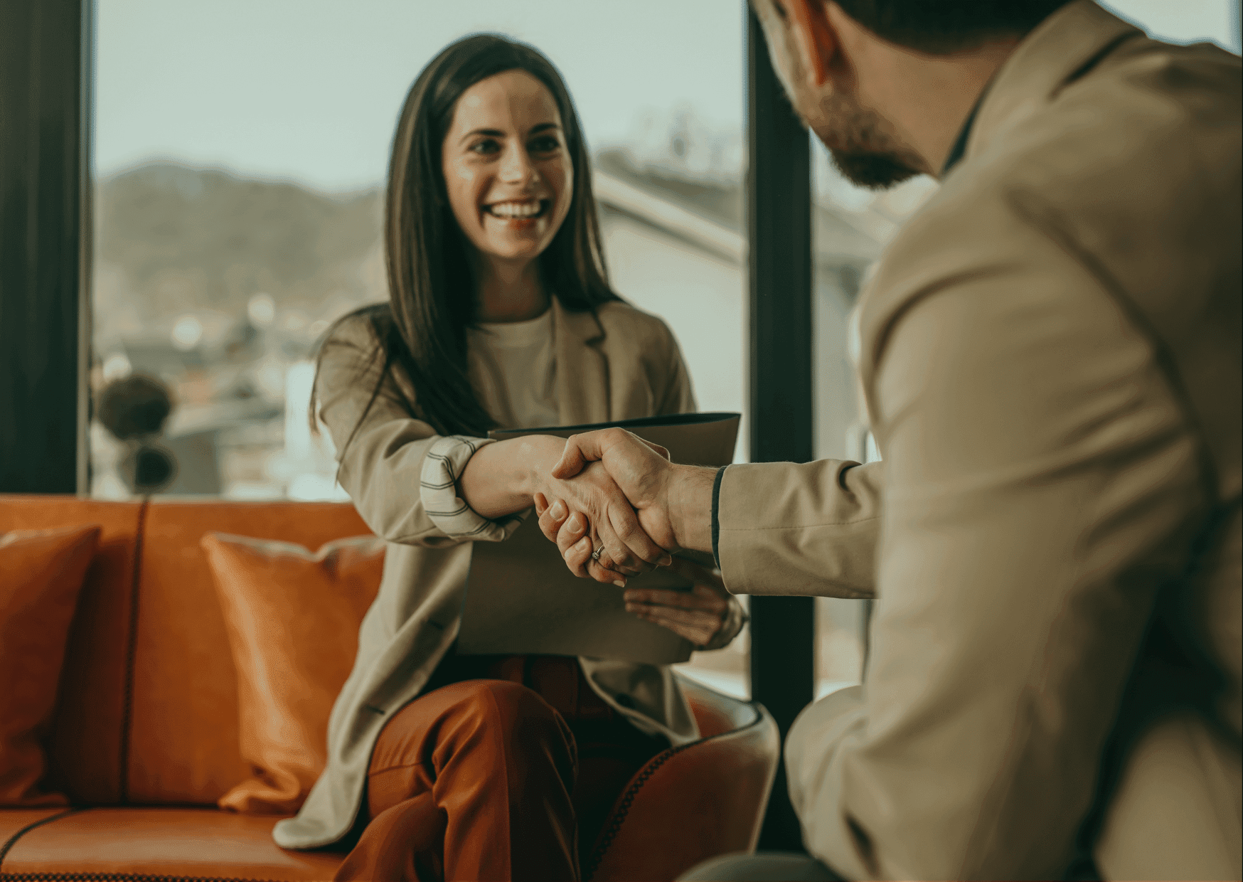 A smiling professional woman shaking hands with a colleague in a bright office lounge to finalize a successful business agreement.
