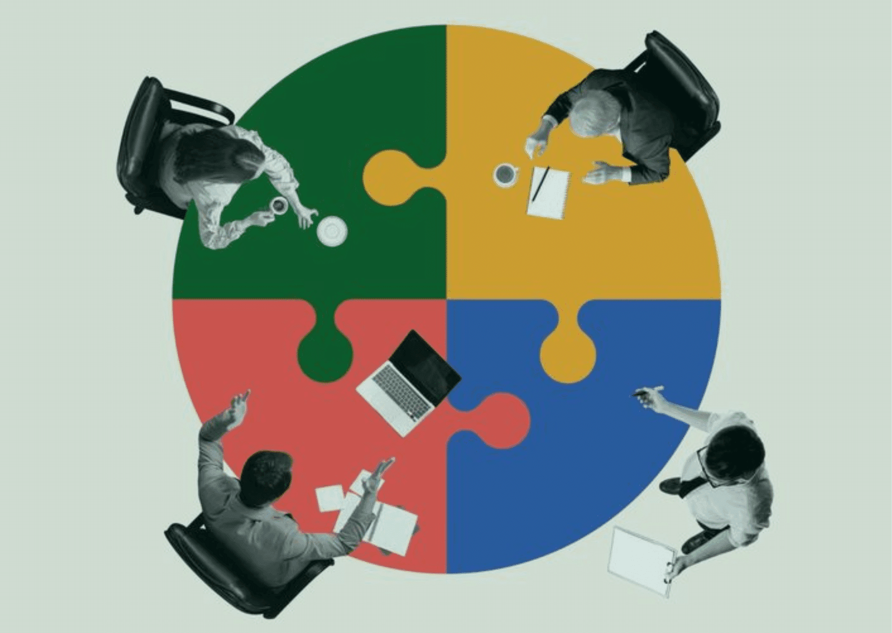 Top-down view of four professionals sitting around a circular table designed as a multi-colored puzzle with green, yellow, red, and blue pieces, symbolizing collaborative teamwork and problem-solving.