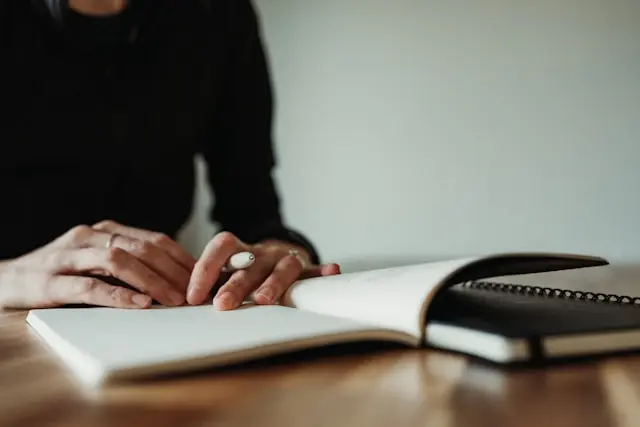 Hands resting on an open notebook on a desk