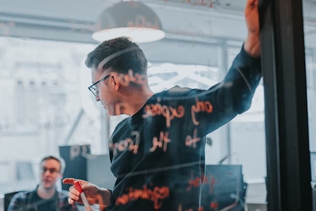 Project professional presenting a plan to colleagues using a glass whiteboard